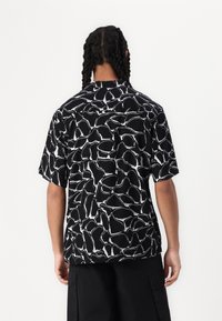 Camicia a maniche corte nera con un motivo astratto bianco, dotata di colletto classico e vestibilità comoda, realizzata in tessuto leggero.