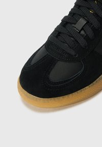 Sorte sneakers med en kombinasjon av semsket skinn og mesh-materialer, med rund tå og gummisåle. Snøringene er mørke og strukturerte.