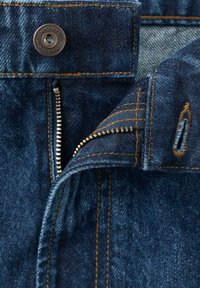 Pantalones vaqueros de mezclilla azul con una cremallera metálica, costuras de cobre y un botón con marca en la cintura. Primer plano de la cremallera y la textura de la tela.