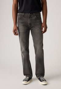 Gray denim jeans with a straight leg, five pockets, and subtle whiskering. Paired with black canvas sneakers featuring white soles.