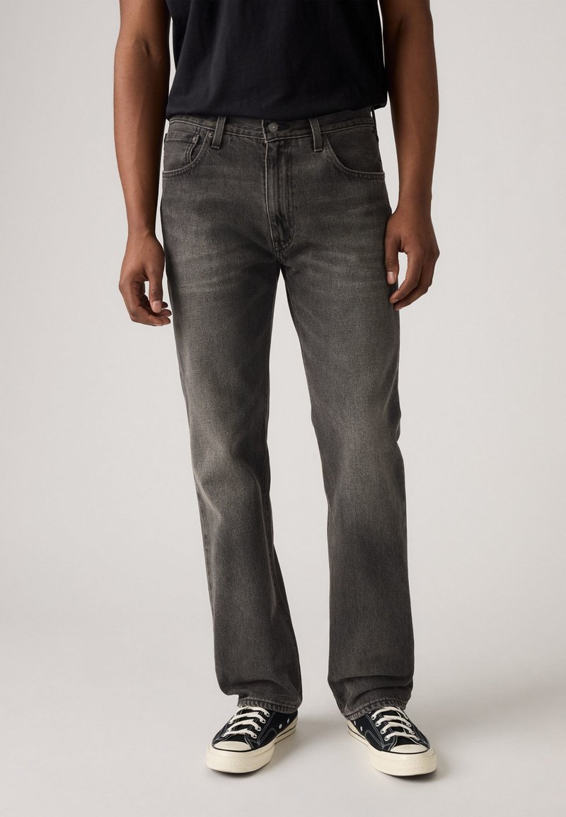 Gray denim jeans with a straight leg, five pockets, and subtle whiskering. Paired with black canvas sneakers featuring white soles.