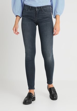 Jeans ajustados de denim oscuro con un diseño entallado, que cuentan con una cintura de media altura, estilo de cinco bolsillos y un ligero desvanecimiento. Combinados con mocasines negros.