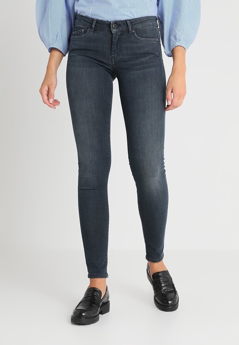 Jeans ajustados de denim oscuro con un diseño entallado, que cuentan con una cintura de media altura, estilo de cinco bolsillos y un ligero desvanecimiento. Combinados con mocasines negros.