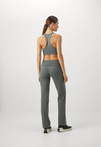 Kvinne som står med ryggen til i en grå racerback sports-bh, matchende høytlivsbukser og svarte joggesko med hvite såler.
