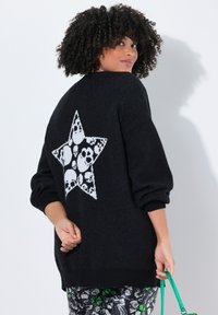 Pull en tricot noir avec un motif d'étoile blanche et des motifs de skulls au dos. Manches longues avec une coupe décontractée et des poignets côtelés.