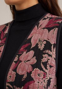 Prsluk s cvjetnim uzorkom na tamnoj pozadini, s ružičastim i burgundskim cvjetovima. Meko tkanje s kontrastnim crnim rubom i detaljima teksture.