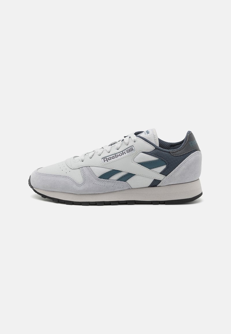 Sneaker Reebok gris clair et bleu marine avec des panneaux en daim et en maille, lacets blancs et semelle noire, présenté en profil droit sur fond blanc.