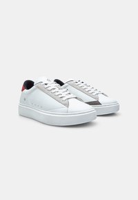 Valged nahast sneakerid hallide seemisnahast aktsentidega, ümar varvas, lame talla ja punane kandmine. Omab toon-toonis õmblusi ja paeltega kinnitust.