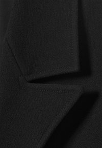 Primer plano del cuello de un abrigo de lana negro con costuras visibles y tejido texturizado.