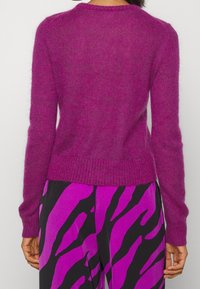 Luddig, rundhalsad tröja i livlig magenta, med ribbad nederkant och ärmar. Buren tillsammans med mönstrade byxor i kompletterande nyanser.