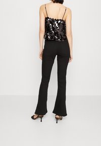 Czarny top z cekinami na regulowanych ramiączkach, w połączeniu z dopasowanymi czarnymi spodniami z szeroką nogawką i czarnymi sandałami na obcasie. Gładka faktura i błyszczące akcenty.