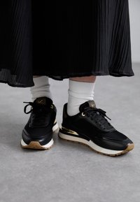 Scarpe sportive nere con accenti dorati, design con lacci e suole in gomma testurizzata. Indossate con calze bianche a crew e una lunga gonna nera plissettata.