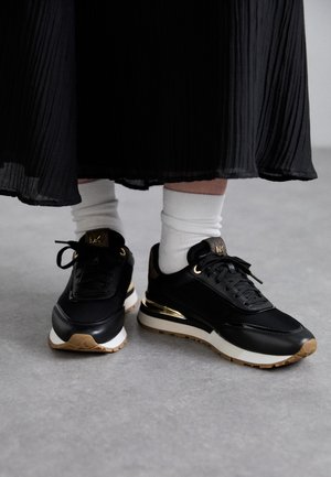 Scarpe sportive nere con accenti dorati, design con lacci e suole in gomma testurizzata. Indossate con calze bianche a crew e una lunga gonna nera plissettata.