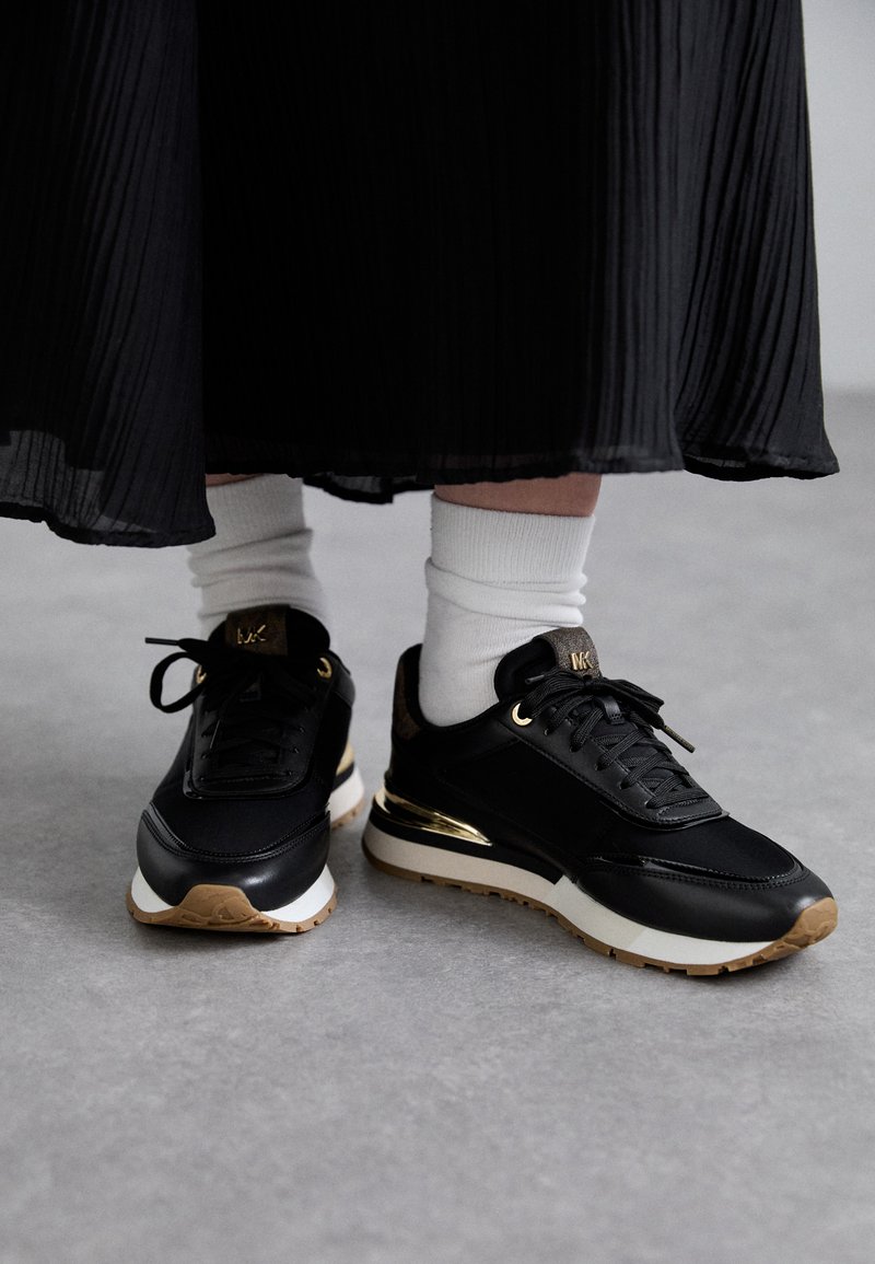 Scarpe sportive nere con accenti dorati, design con lacci e suole in gomma testurizzata. Indossate con calze bianche a crew e una lunga gonna nera plissettata.