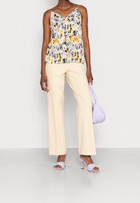 Ärmlös, flerfärgad blommig topp med V-ringning; krämfärgade vida byxor; lavendelfärgad handväska; ljuslila klacksandaler.