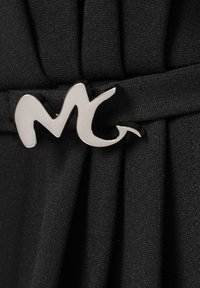 Tessuto nero con pieghe e una chiusura decorativa metallica argento con design astratto, che ricorda la lettera "M".