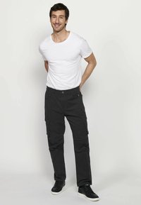 Zwarte cargobroeken met meerdere zijzakken, gecombineerd met een aangesloten wit T-shirt. Het model draagt zwarte sneakers. Eenvoudig, casual ontwerp.