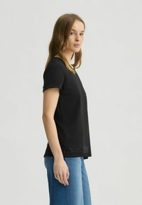 Top nero a maniche corte con scollatura rotonda, caratterizzato da un sottile dettaglio testurizzato vicino all'orlo. Abbinato a jeans a gamba larga blu chiaro.