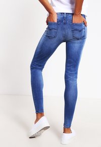 Jeans de denim azul ajustados con cintura de media altura, diseño de cinco bolsillos y desvanecimiento mínimo. Cuenta con bolsillos traseros con un detalle de costura sutil.