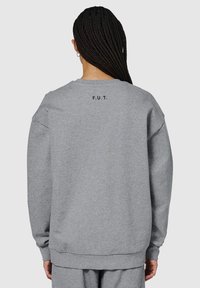 Grijze sweatshirt met een relaxte pasvorm, lange mouwen, ribbelboorden en een ribbelrand. Heeft "F.U.T." gedrukt op de achterkant onder de halslijn.