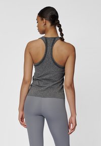 Szary sportowy top na ramiączkach z fasonem racerback, wykonany z teksturowanej tkaniny z kontrastującym szwem. Połączony z jasnoszarymi legginsami.
