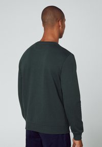 Sudadera de color verde oscuro con mangas largas, cuello redondo y puños acanalados. Textura suave; diseño minimalista sin patrones o acentos visibles.
