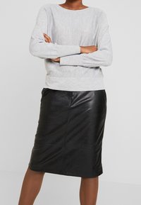 Maglione grigio chiaro con scollatura rotonda e polsini a coste abbinato a una gonna a tubino in pelle nera caratterizzata da una superficie liscia e una cucitura frontale.