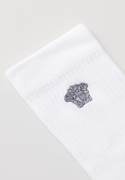 Weiße Socke mit strukturiertem Strick, versehen mit einem grauen gestickten Logo am Bund. Das Material wirkt weich und atmungsaktiv.