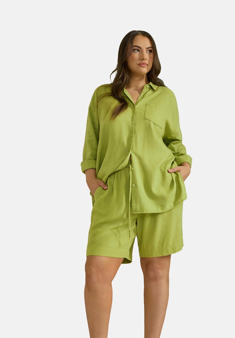 Camicia di lino verde lime con tasca frontale e maniche arrotolate, abbinata a pantaloni shorts coordinati con vita regolabile tramite cordoncino.