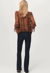 Brązowa kwiecista bluzka z rozszerzanymi rękawami, przezroczystym materiałem i warstwowym krojem, zestawiona z ciemnymi rozszerzanymi dżinsami i czarnymi szpilkami.