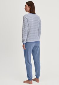 Gestreiftes Langarmoberteil in Blau und Weiß, kombiniert mit einfarbigen blauen Jogginghosen. Der Stoff wirkt weich und bequem mit elastischen Bündchen.