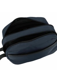 Neceser de color azul marino con una textura suave, que cuenta con múltiples compartimentos con cremallera y una forma redondeada. Las cremalleras son de color negro.