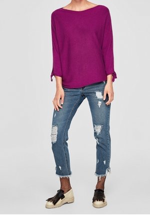 Haut violet à manches trois-quarts avec un décolleté bateau. Porté avec un jean bleu clair déchiré, présentant un ourlet effiloché et des chaussettes en résille dans les chaussures.