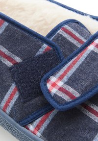 Chausson à carreaux bleus avec un intérieur doux, fermeture à bande Velcro et matériau extérieur texturé avec des rayures rouges et blanches.