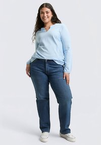 Ljusblå ribbad tröja med långa ärmar och v-ringning, matchad med mörkblå jeans med raka ben och vita sneakers. Enkel, avslappnad outfit.