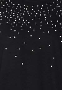 Top negro con un arreglo de perlas blancas y piedras de strass transparentes de diferentes tamaños, creando un patrón decorativo a lo largo de la tela.
