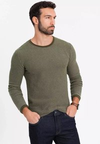 Olivgrünes Langarmstrickshirt mit einem strukturierten Muster, Rundhalsausschnitt und kontrastierenden Manschetten, kombiniert mit dunkelblauen Jeans.