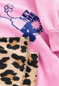 Lyserød sweatshirt med blåt grafisk tekst og blomsterdesign; beige stof med sort leopardprint og rynket kant nederst.