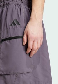 Grå idrottsshorts med elastisk midja, sidoficka med svart dragkedja och en svart Adidas-logga på framsidan.