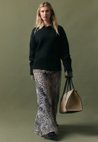 Zwarte gebreide trui met geribde boorden, gedragen over een olijfgroene shirt. Vloeiende, doorschijnende, dierenprint broek. Beige handtas met zwarte handvatten.