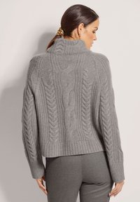 Grauer gestrickter Pullover mit hochgestelltem Kragen, der aus Zopfstrickmustern besteht, überschnittenen Schultern und einem kurzen Design. Weiche Textur.
