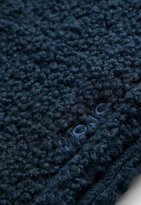 Tissu texturé bleu marine avec une surface en boucles. Présente un subtil détail de broderie bleue le long d'un bord.