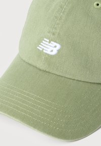 Ανοιχτό πράσινο καπέλο baseball με λευκό κεντημένο λογότυπο New Balance στην μπροστινή πλευρά, απεικονιζόμενο σε απλό λευκό φόντο.