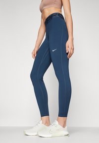 Námořnické modré sportovní legíny s vysokým pasem, které mají černý nápis "PRO", hladkou texturu a bílý logo Nike na levém stehně.