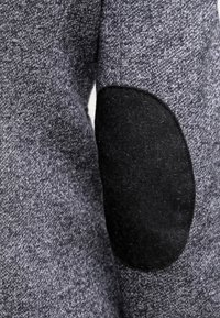 Grijze gebreide stof met een gladde textuur, voorzien van een zwarte elleboogpatch made van een iets fuzzy materiaal.