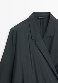 Dunkelgrauer Blazer mit lockerer Passform, Reverskragen und elegantem Stoff, der minimale Nahtdetails und einen unsichtbaren Reißverschluss auf der Rückseite aufweist.