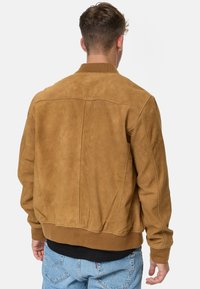 Suede bomber jacket in camel brown, featuring ribbed collar and cuffs, with a smooth texture and simple stitching details.