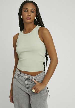 Débardeur côtelé vert clair avec un col rond, associé à un jean gris taille haute. Détails notables : fermeture à boutons et tissu texturé.