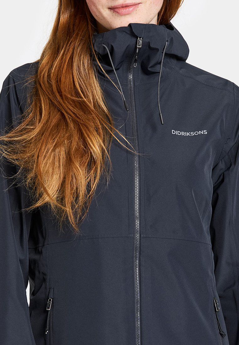 Marineblaue wasserdichte Jacke mit hohem Kragen, Reißverschluss, verstellbaren Tunnelzügen und Seitentaschen. Mit "Didriksons"-Logo auf der Brust.