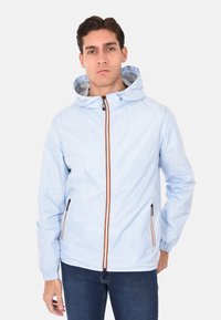 Giacca impermeabile azzurro chiaro con zip frontale, dettagli della zip arancioni e cappuccio. Presenta polsini elasticizzati e tasche laterali con zip.